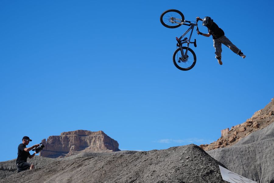 A mountain biker throwing a no-footer over a dirt jump as a filmer shoots from below