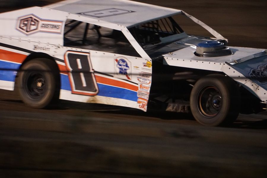 A number 8 modified race car sliding through a dirt-track turn at dusk