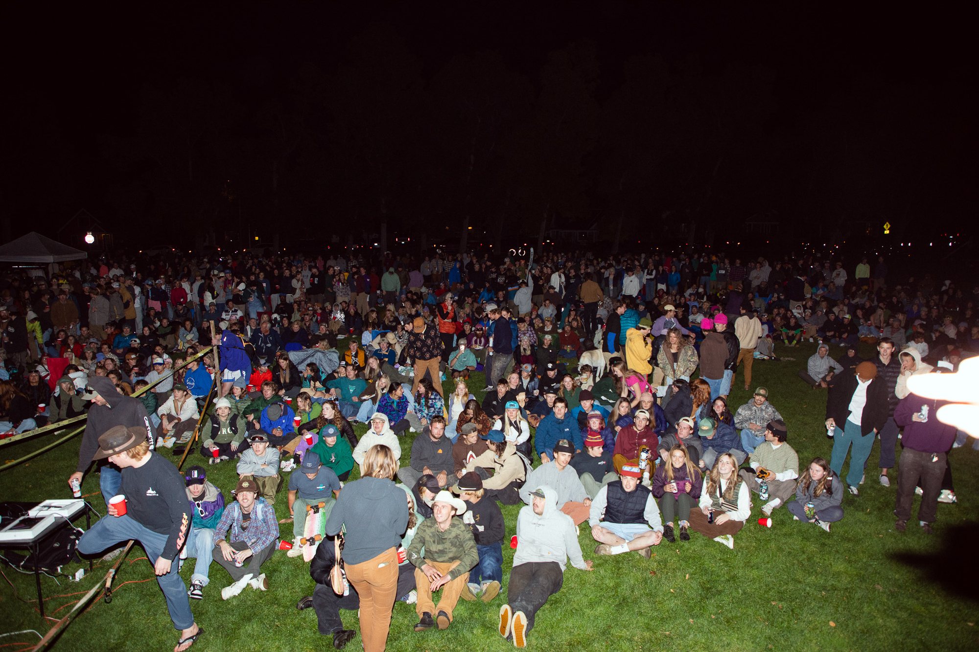 A large crowd sitting on the grass at night at a Montana Bandits ski film premiere in a Bozeman park
