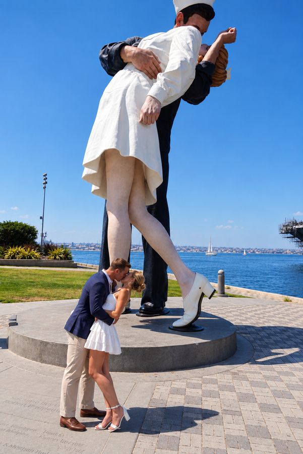 A newly engaged couple kissing beneath the giant statue on the San Diego waterfront