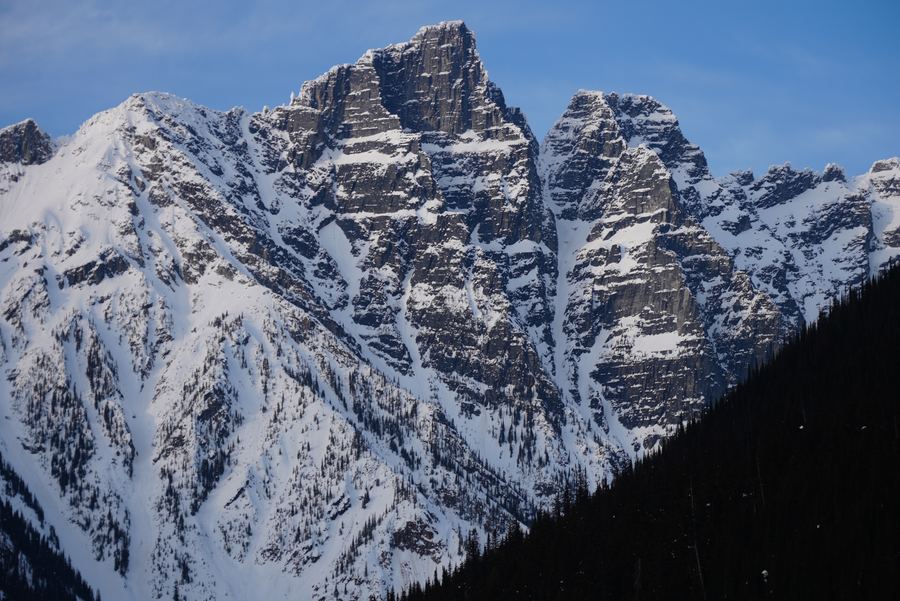 Sheer granite peaks plastered in snow above a dark forested slope